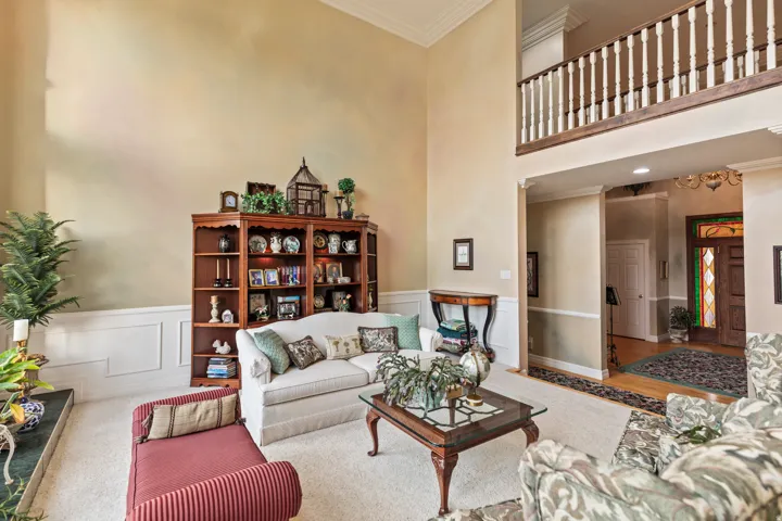 Living room with ornamental molding, a decorative wall, a wainscoted wall, and a high ceiling