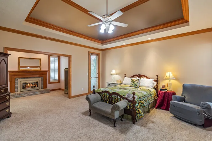 Bedroom with a fireplace, light colored carpet, a raised ceiling, ceiling fan, and ornamental molding