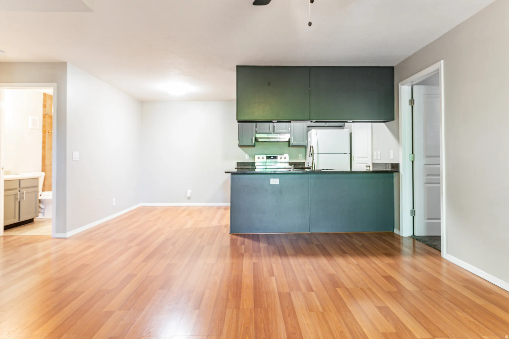 Open-concept living space featuring wood-finish flooring, a kitchen island with dark cabinetry, a white refrigerator, and a white electric range