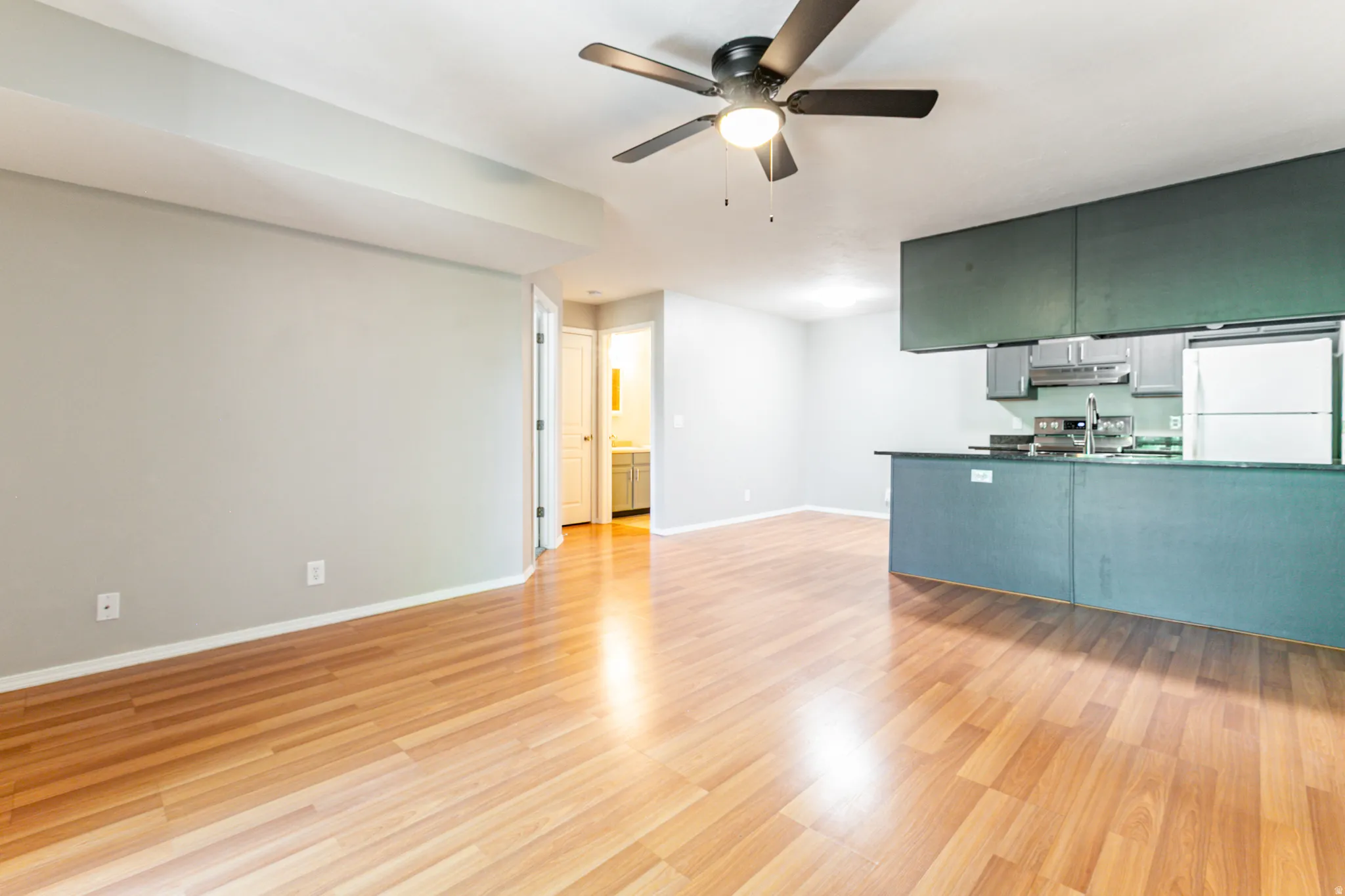 Open concept living area featuring wood-finish flooring, a ceiling fan, and a kitchen with dark cabinetry and a breakfast bar