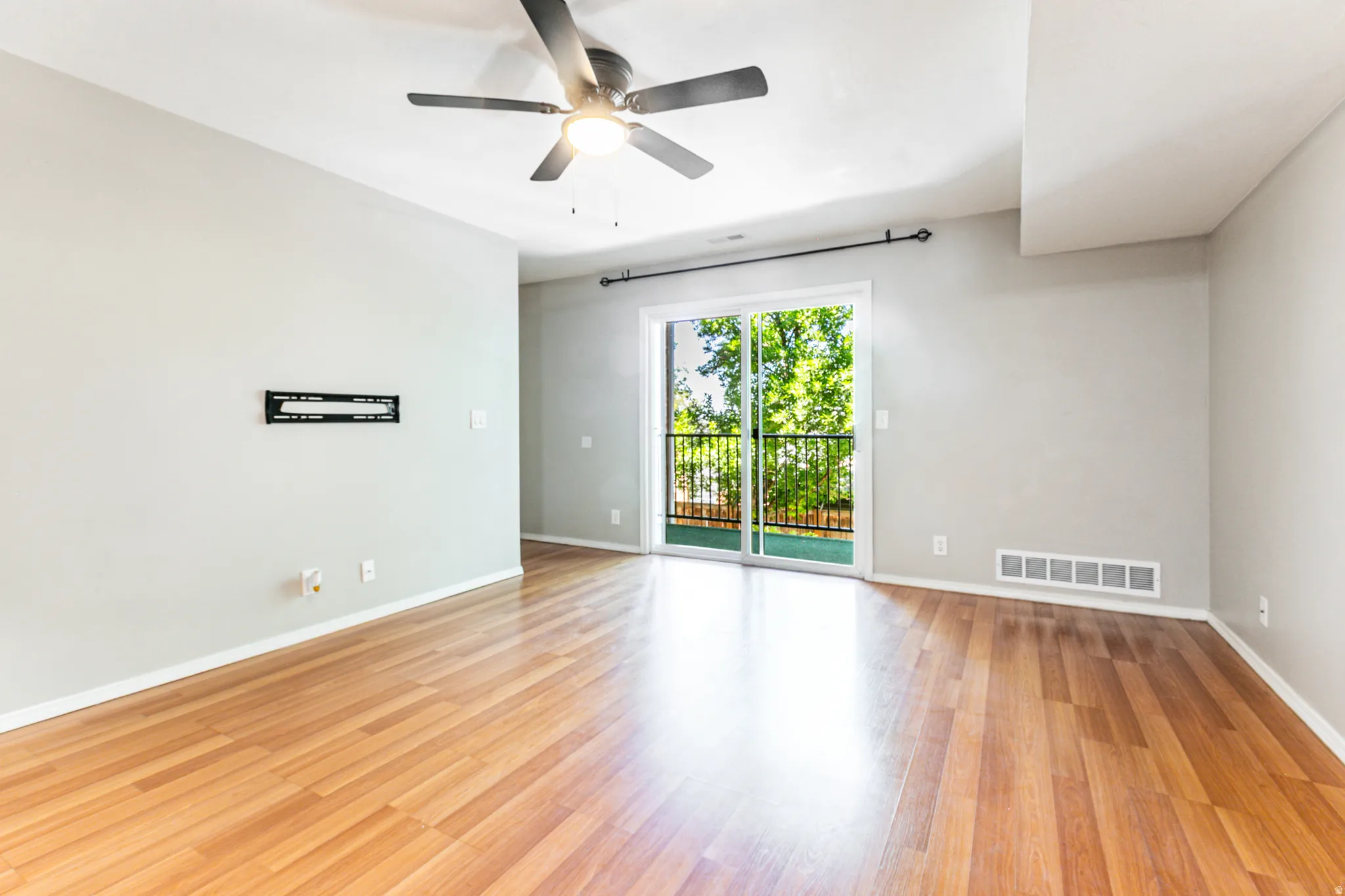 Open living space featuring wood-finish flooring, a ceiling fan with integrated lighting, and light gray wall tones