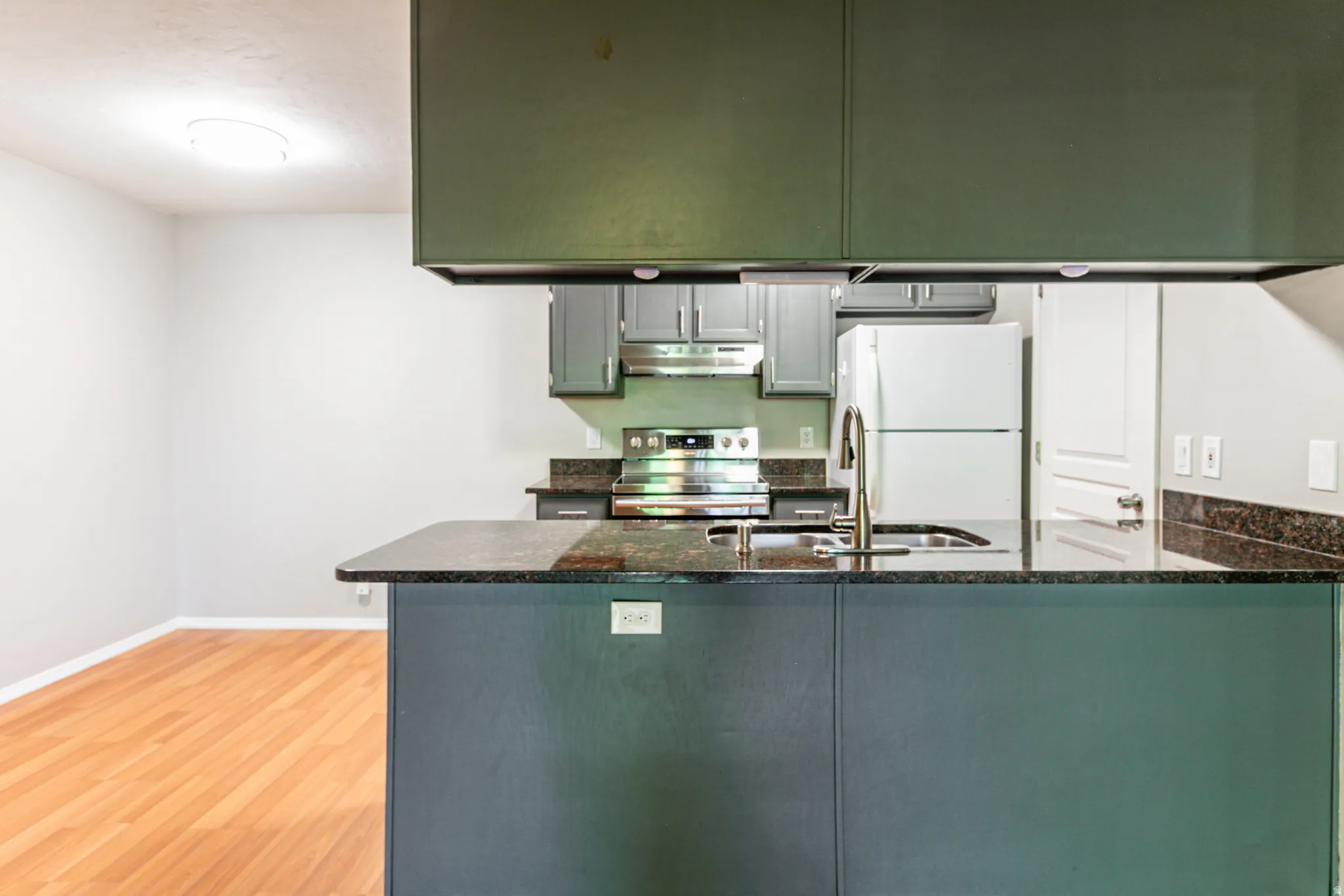 Kitchen island featuring dark cabinetry and a stone-finish countertop with an undermount sink and stainless steel faucet