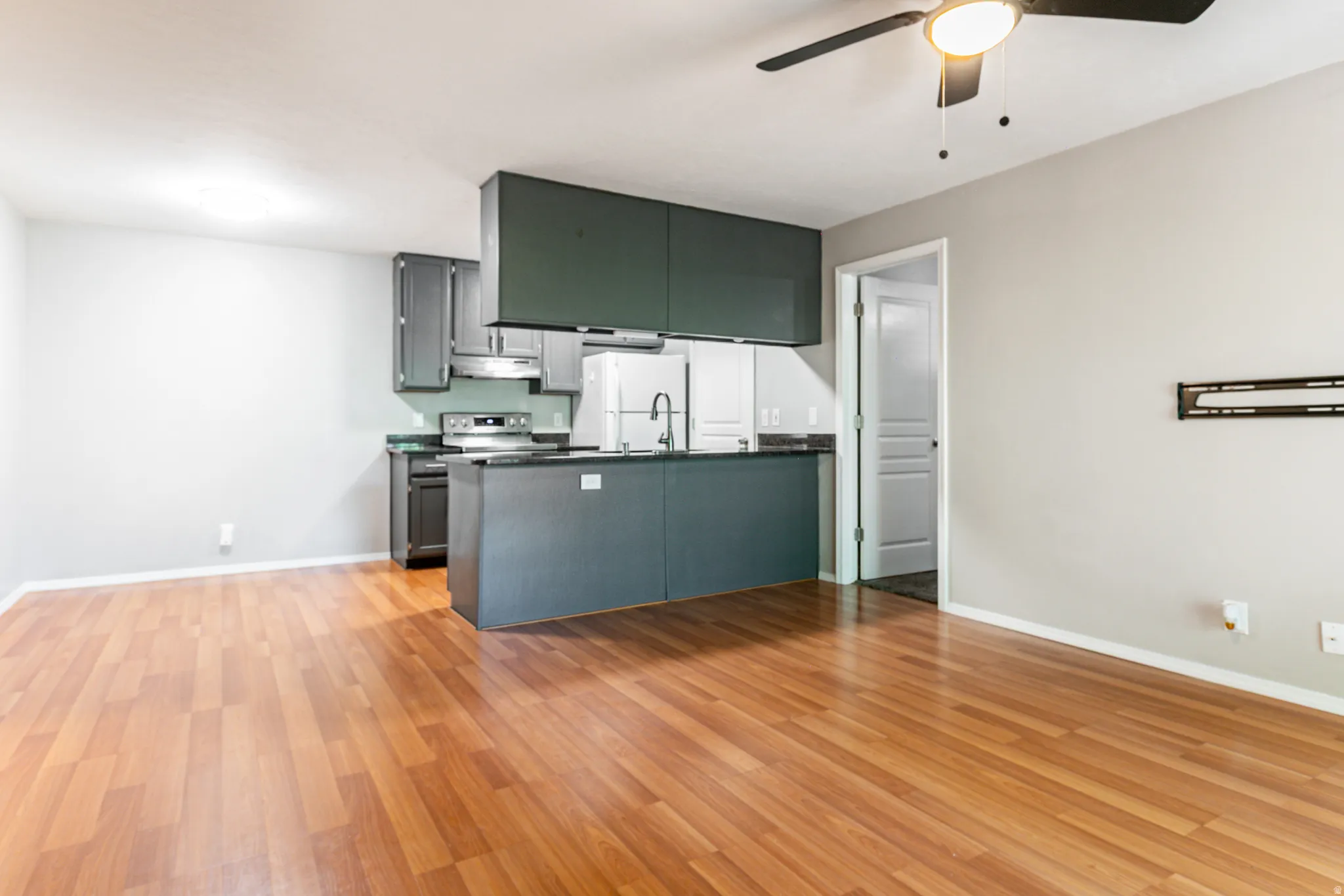 Open-concept living space featuring wood-finish flooring, a ceiling fan with integrated lighting, and a kitchen island with built-in storage