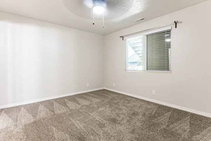 Neutral-toned room featuring a window with horizontal blinds, a ceiling fan with integrated lighting, and plush grey carpeting