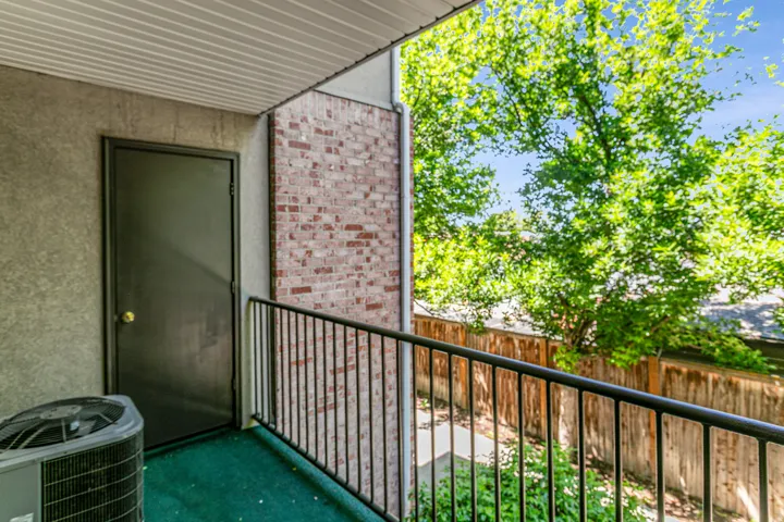 Balcony with brick wall accents, black metal railing, and green outdoor carpeting