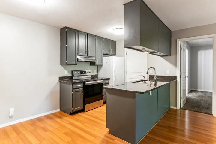Kitchen featuring dark gray cabinetry, stainless steel range and range hood, a breakfast bar, dark countertops, and wood-finish flooring