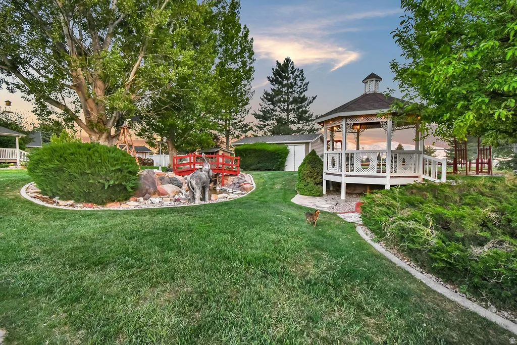 Expansive backyard featuring a white gazebo with decorative railings, a detached storage shed, and mature trees providing shade