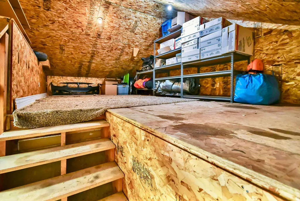 Upper-level storage area featuring wood-finish walls and ceiling, carpeted flooring on a raised platform, and built-in shelving