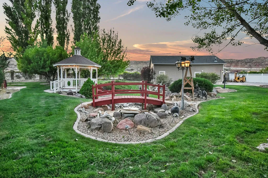 Expansive landscaped lawn featuring a decorative white gazebo with built-in lighting, a red ornamental bridge, and a rock garden with a water feature