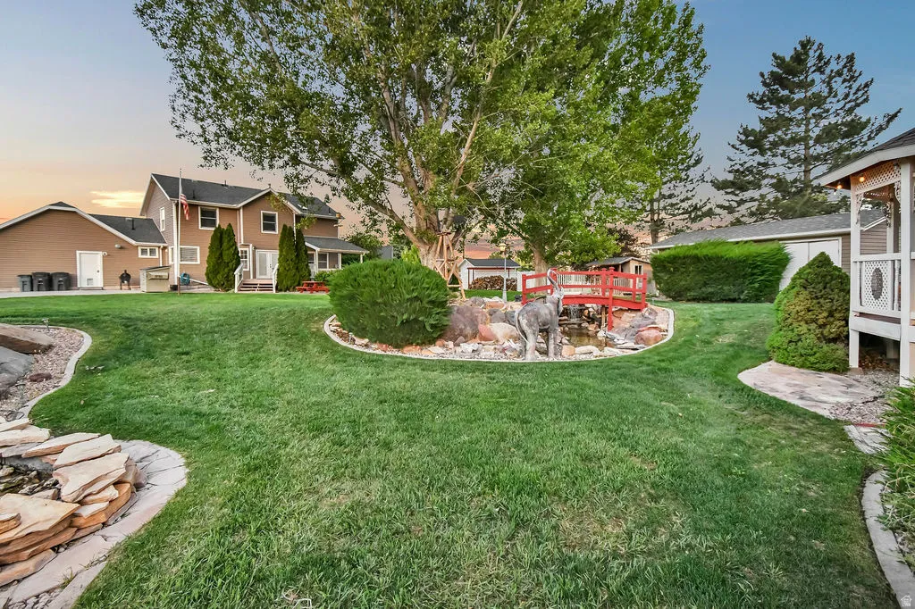 Expansive green lawn with a rock-lined water feature, a small red footbridge, and a detached gazebo