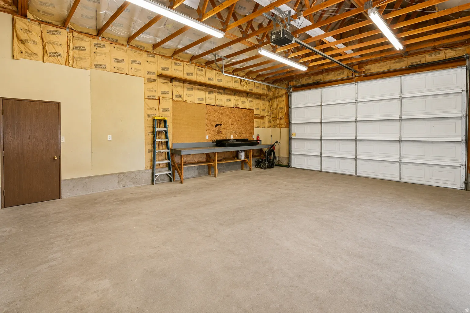 Spacious garage featuring a large paneled door, exposed ceiling joists, and fluorescent lighting fixtures