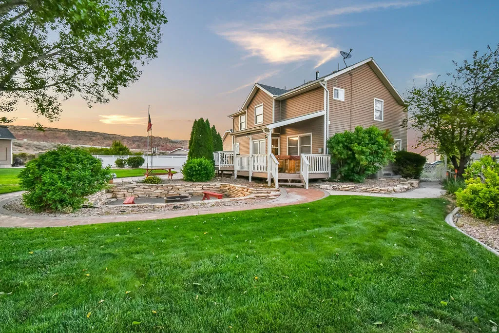 Expansive green lawn with a stone-lined fire pit area, a multi-level deck, and mature landscaping