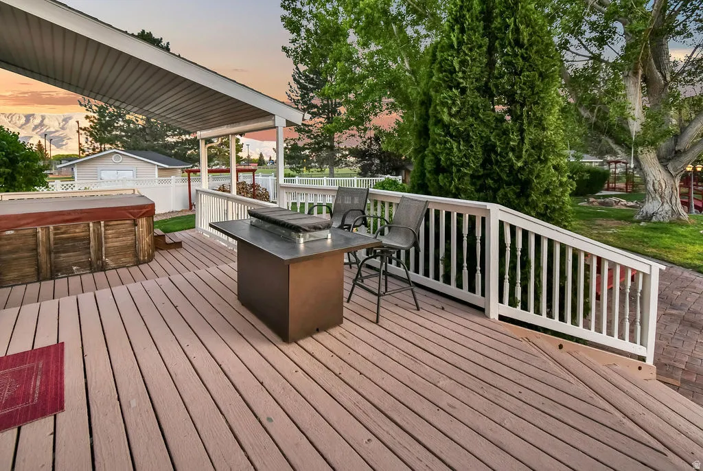 Expansive wood-finish deck featuring a covered patio, white baluster railing, and a built-in hot tub