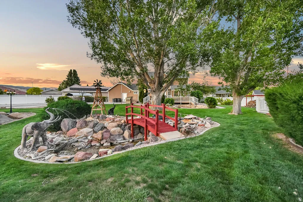 Sprawling green lawn featuring mature trees and a decorative rock-lined water feature with a red pedestrian bridge