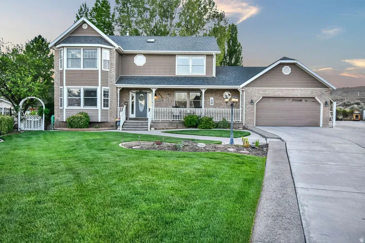 Traditional-style residence featuring a two-car garage, expansive front lawn, welcoming covered porch with white railings, and a decorative garden archway