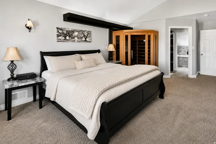 Spacious bedroom featuring light neutral wall paint, vaulted ceiling, and plush neutral carpeting