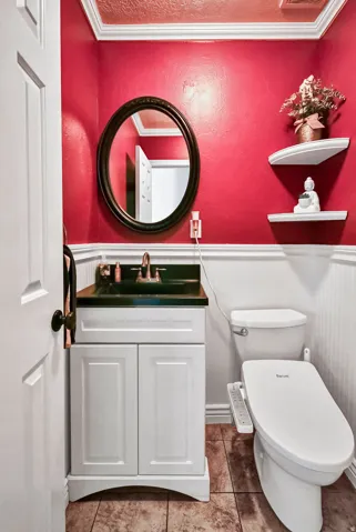 Bathroom featuring a white vanity with panel-front cabinetry and dark countertop, a wall-mounted oval mirror, and tile flooring