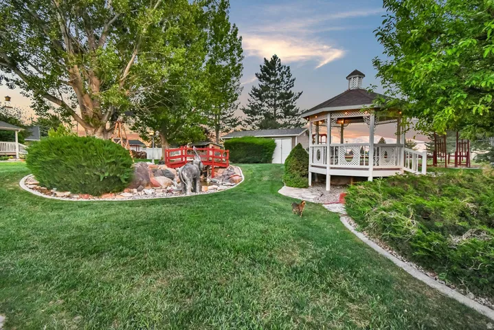 Expansive backyard featuring a white gazebo with decorative railings, a detached storage shed, and mature trees providing shade