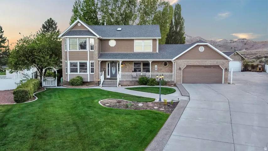Two-story residence featuring brick and siding exterior, a covered front porch with white railings, an attached two-car garage, and a concrete driveway