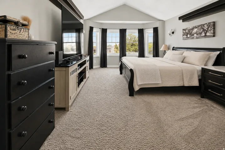 Vaulted ceiling bedroom with a bay window, carpeted flooring, and a ceiling-mounted light fixture