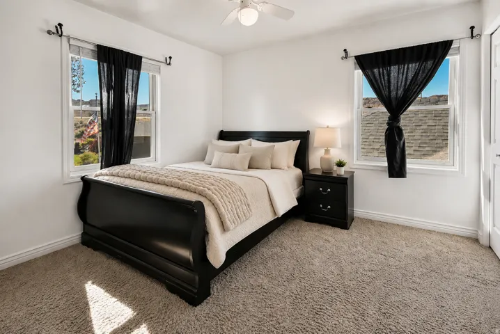 Bright bedroom featuring plush carpeting, two windows with contrasting dark drapery, and a ceiling fan North West