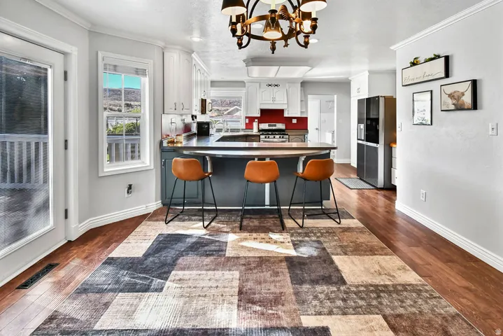 Spacious kitchen featuring a dark countertop island with seating, wood-finish flooring, white cabinetry, a red tile backsplash, and a glass-paneled door leading to an outdoor deck