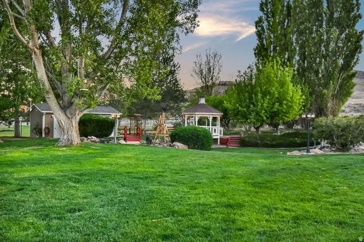 Expansive green lawn featuring mature trees, a detached shed, and a white gazebo with red steps