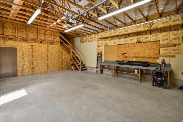 Spacious garage featuring a concrete floor, exposed wood beam ceiling, and a built-in staircase
