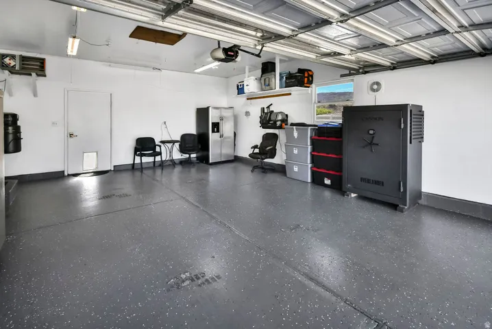 Spacious garage featuring a durable epoxy floor coating, white painted walls, overhead storage shelving, and a window providing natural light