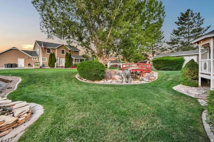 Expansive green lawn with a rock-lined water feature, a small red footbridge, and a detached gazebo