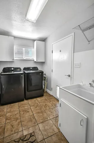 Utility room featuring durable tile flooring, a utility sink with white cabinetry, upper white storage cabinets, and a window with horizontal blinds