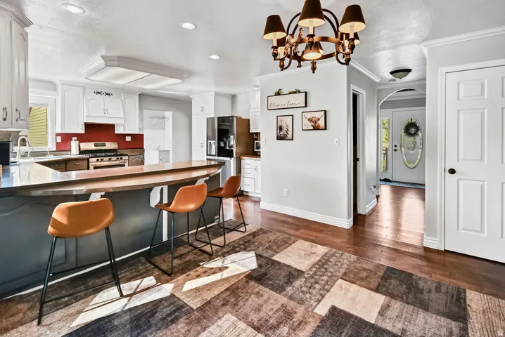 Open-concept kitchen featuring white cabinetry, a dark countertop with a breakfast bar, and a stainless steel gas range