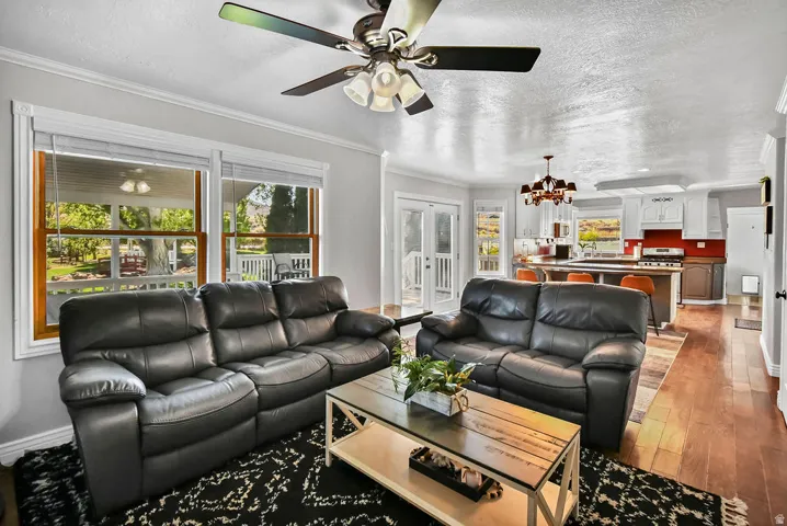 Open-concept living space featuring wood-finish flooring, a ceiling fan with integrated lighting, and multiple windows with wood trim