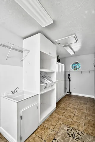 Utility room featuring a built-in sink with cabinetry, extensive white storage cabinetry and shelving, wire shelving, and a tiled floor
