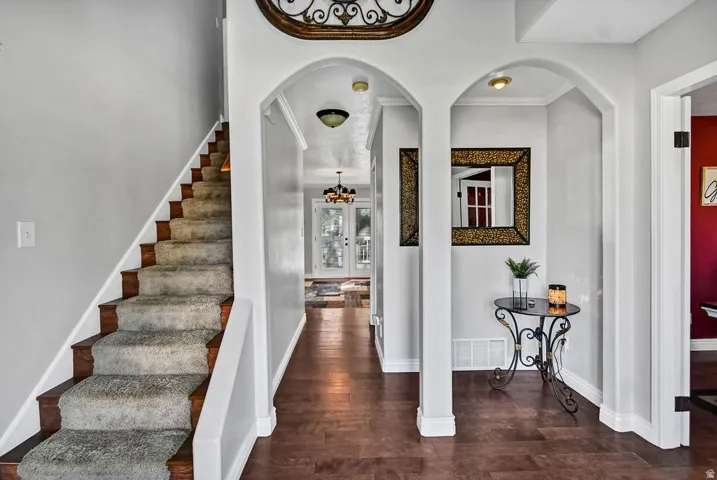 Entryway featuring rich wood-finish flooring, a carpeted staircase with wood risers, arched doorways, and light gray walls