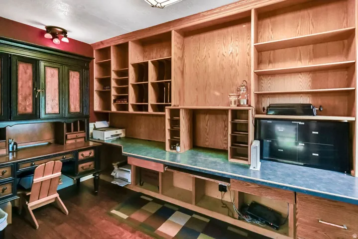 Built-in office cabinetry and shelving in warm wood tones, featuring a dark wood-finish desk with storage drawers