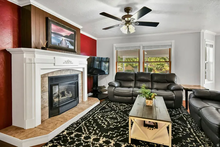 Living room featuring a decorative fireplace with a tile surround and hearth, white mantelpiece, ceiling fan, and multiple windows