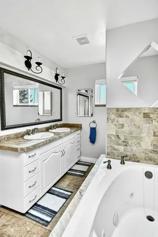 Bathroom featuring a dual vanity with white cabinetry and a stone-look countertop, two undermount sinks, and an oversized framed mirror