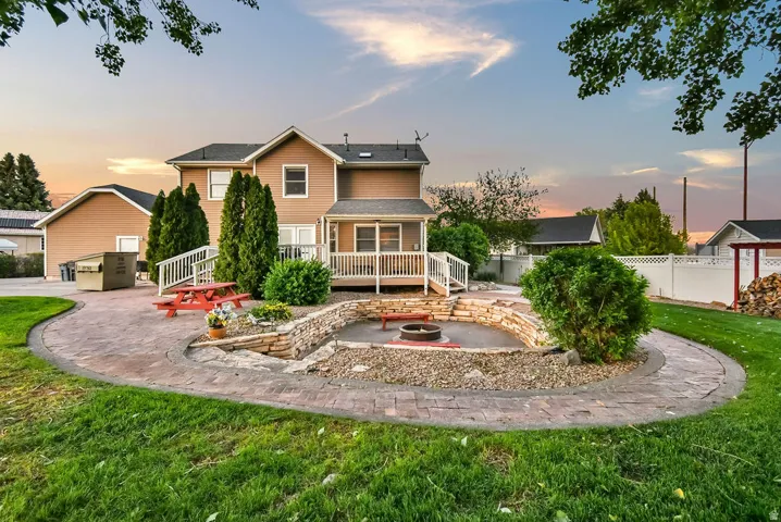 Expansive backyard featuring a stamped concrete patio, built-in fire pit with stone retaining wall, and a deck with white railings