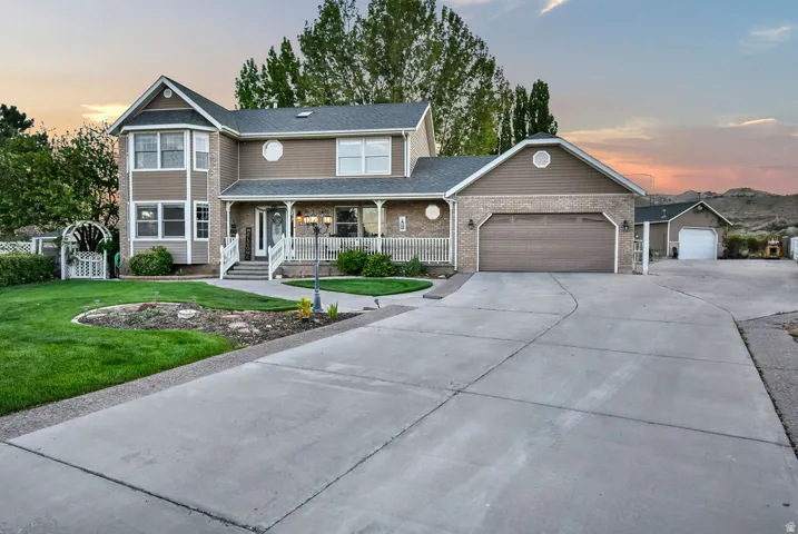Multi-story residence featuring a covered front porch with white railing, brick and siding exterior, two-car attached garage, a detached single-car garage, and a concrete driveway