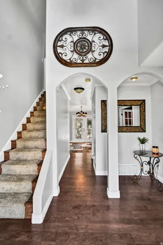 Foyer featuring dark wood-finish flooring, a carpeted staircase with wood risers, arched doorways, and white baseboards