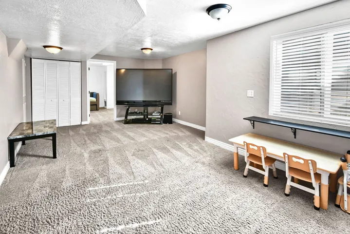 Spacious room featuring textured carpeting, neutral wall finishes, and a window with blinds