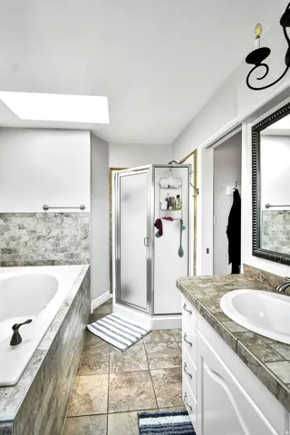 Spacious bathroom featuring a white soaking tub with tiled surround, an enclosed shower, and a vanity with a white basin and tiled countertop
