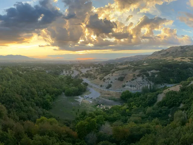 Expansive valley and mountain scenery, featuring lush green foliage, distant urban areas, and a multi-story building