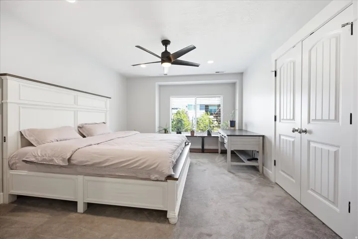 Carpeted bedroom featuring white paneled closet doors with dark hardware, recessed lighting, and a modern ceiling fan