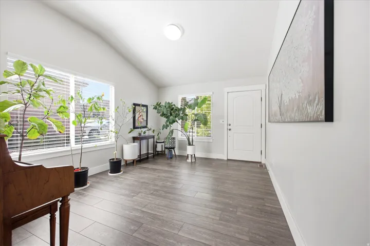 Spacious entryway featuring high vaulted ceilings, large windows with blinds, wood-finish flooring, and a paneled entry door