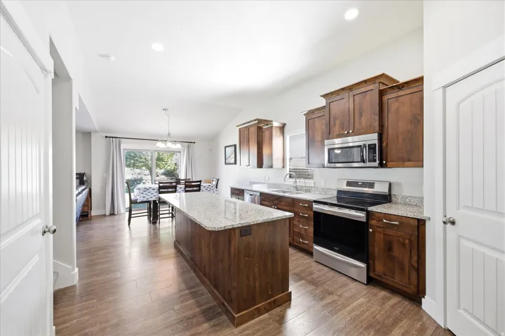 Open-concept kitchen featuring an island with granite countertops, stainless steel appliances, wood-finish flooring, and ample cabinetry