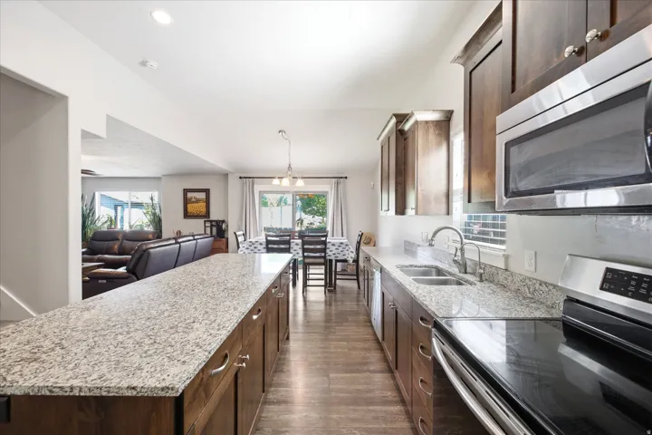 Modern kitchen featuring stone countertops, dark wood cabinetry, stainless steel appliances, and wood-finish flooring