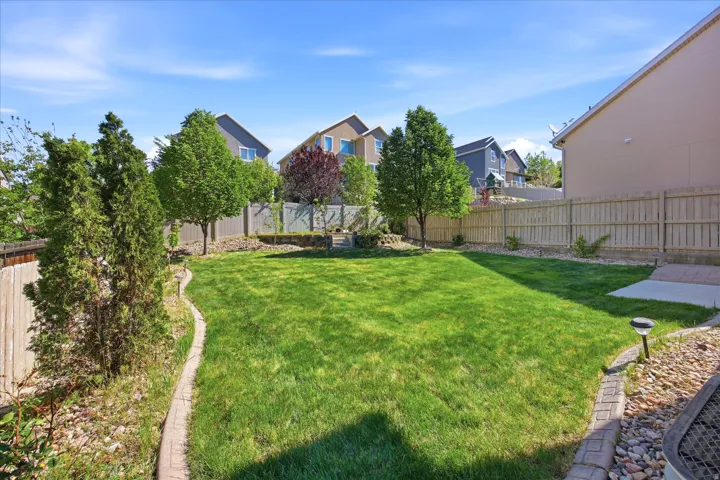 Expansive backyard featuring a manicured lawn, established trees, a paver stone border, and a concrete patio pad