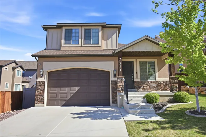 Contemporary stucco exterior featuring stone accents, an attached garage, a covered front porch, and a concrete driveway